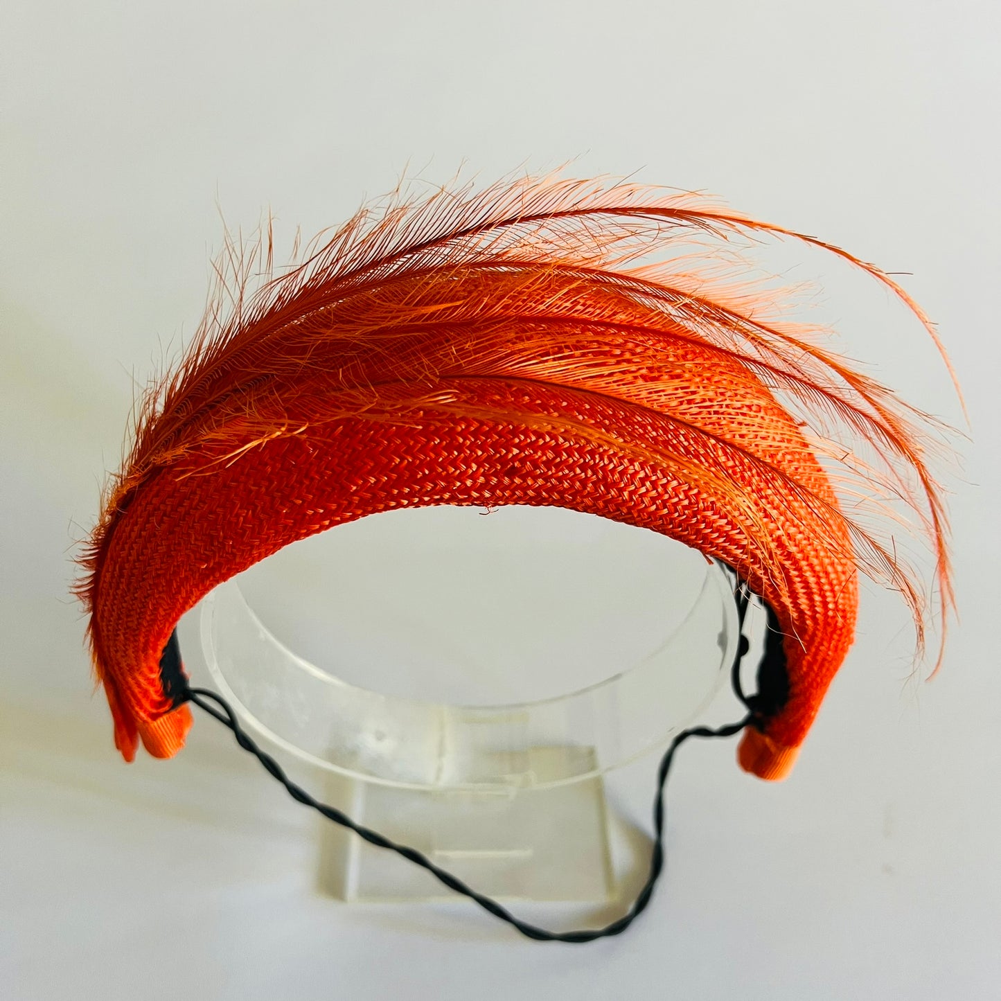 An orange straw padded headband finished with delicate feather trim
