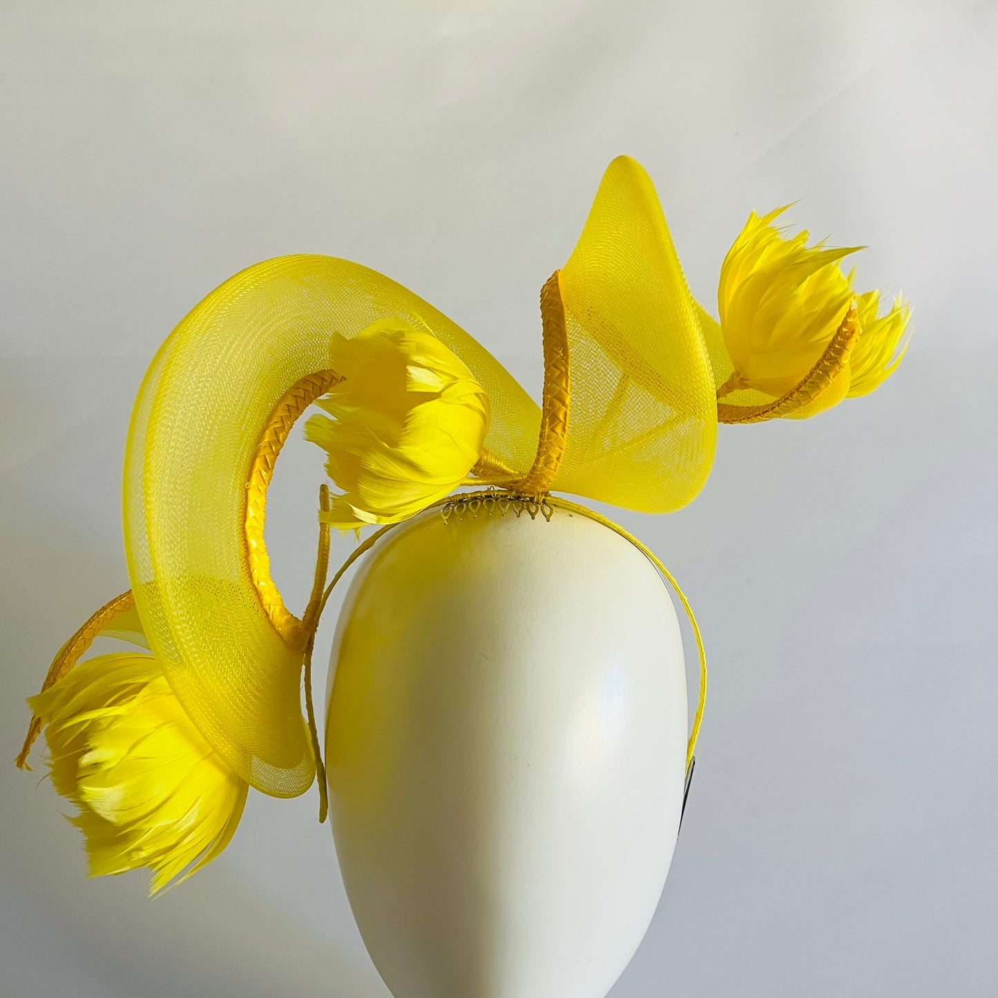 A vibrant headband featuring a swirl of crinoline and handmade feather flowers, all in bright yellow for a striking finish.