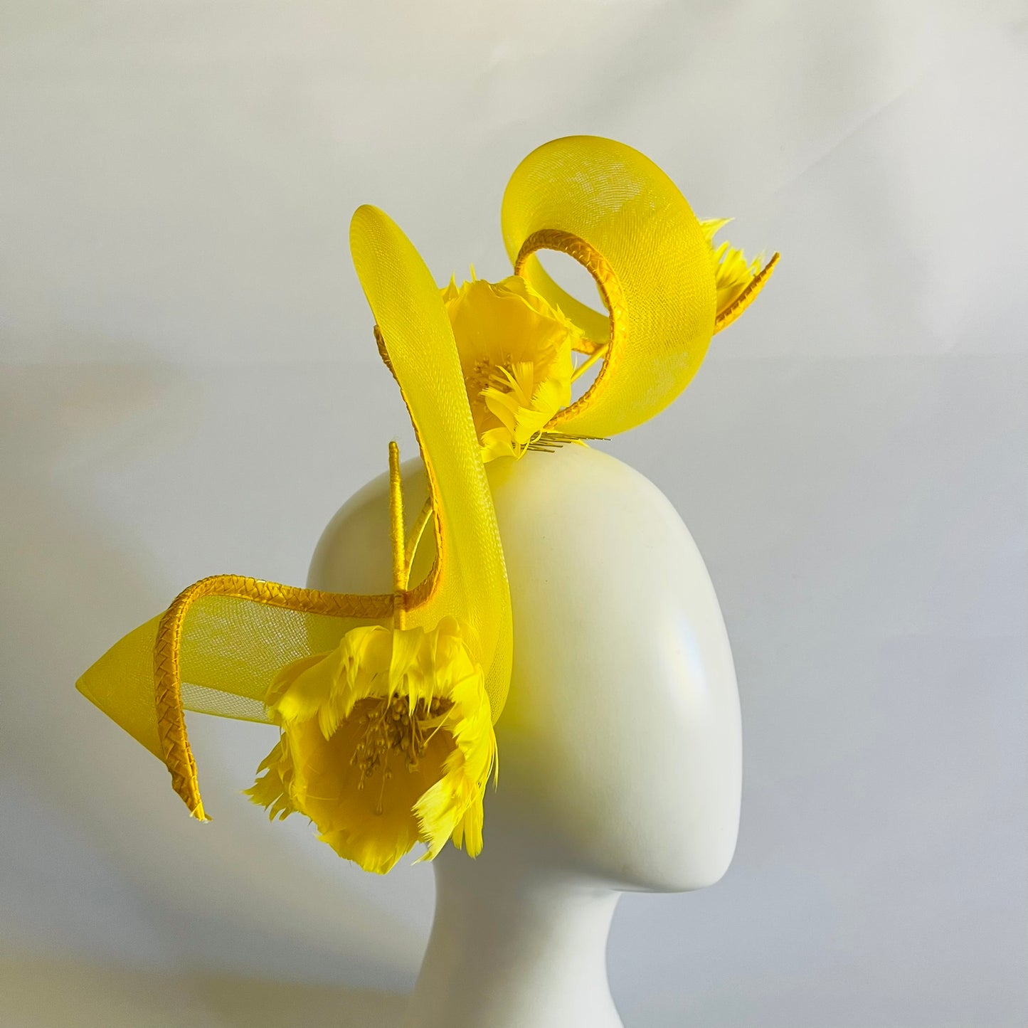 A vibrant headband featuring a swirl of crinoline and handmade feather flowers, all in bright yellow for a striking finish.